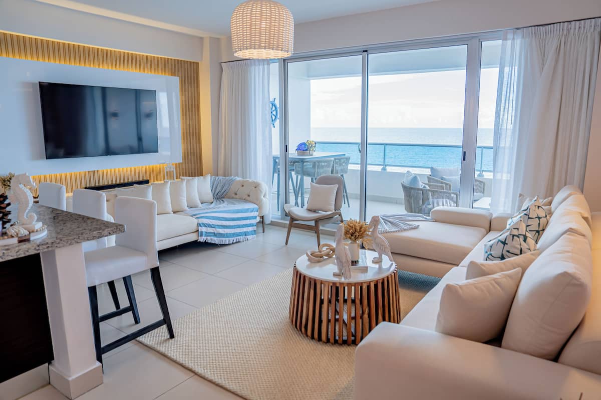 Ein modernes Wohnzimmer mit Flachbildfernseher, Essbereich und Balkon mit Meerblick.