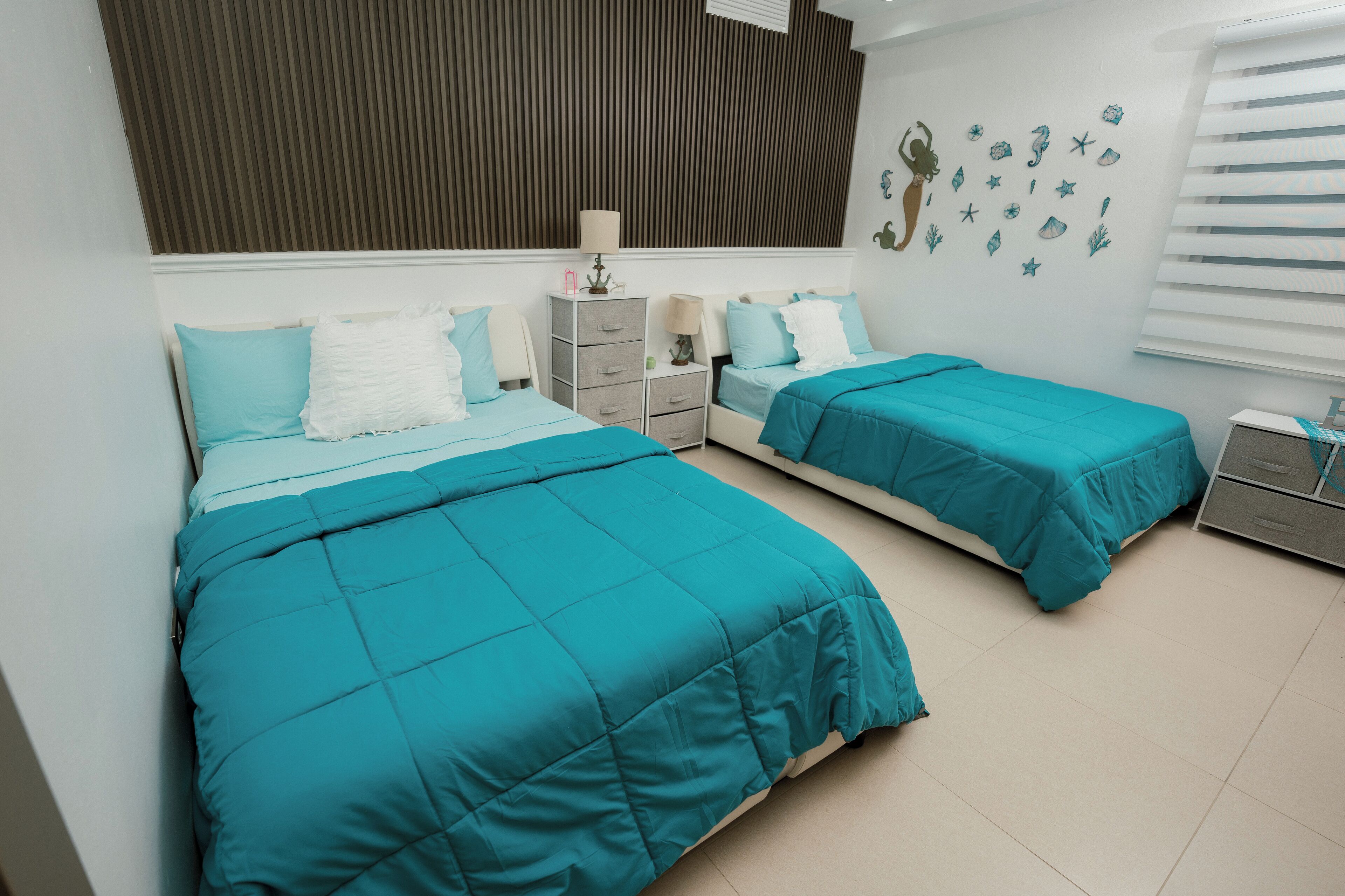 Camera da letto con due letti, ognuno con biancheria verde acqua, una cassettiera e un muro decorato con adesivi a tema marino.