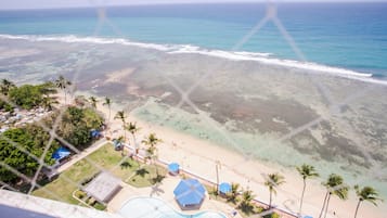 Resort à beira-mar com piscina, guarda-sóis e palmeiras.