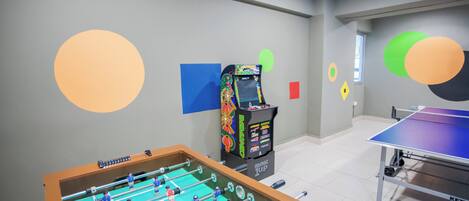 A room with a foosball table, a ping pong table, and a foosball machine.