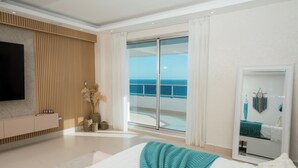 Une chambre moderne avec un grand lit, une télévision, une porte-fenêtre coulissante donnant sur un balcon et une vue sur l’océan.