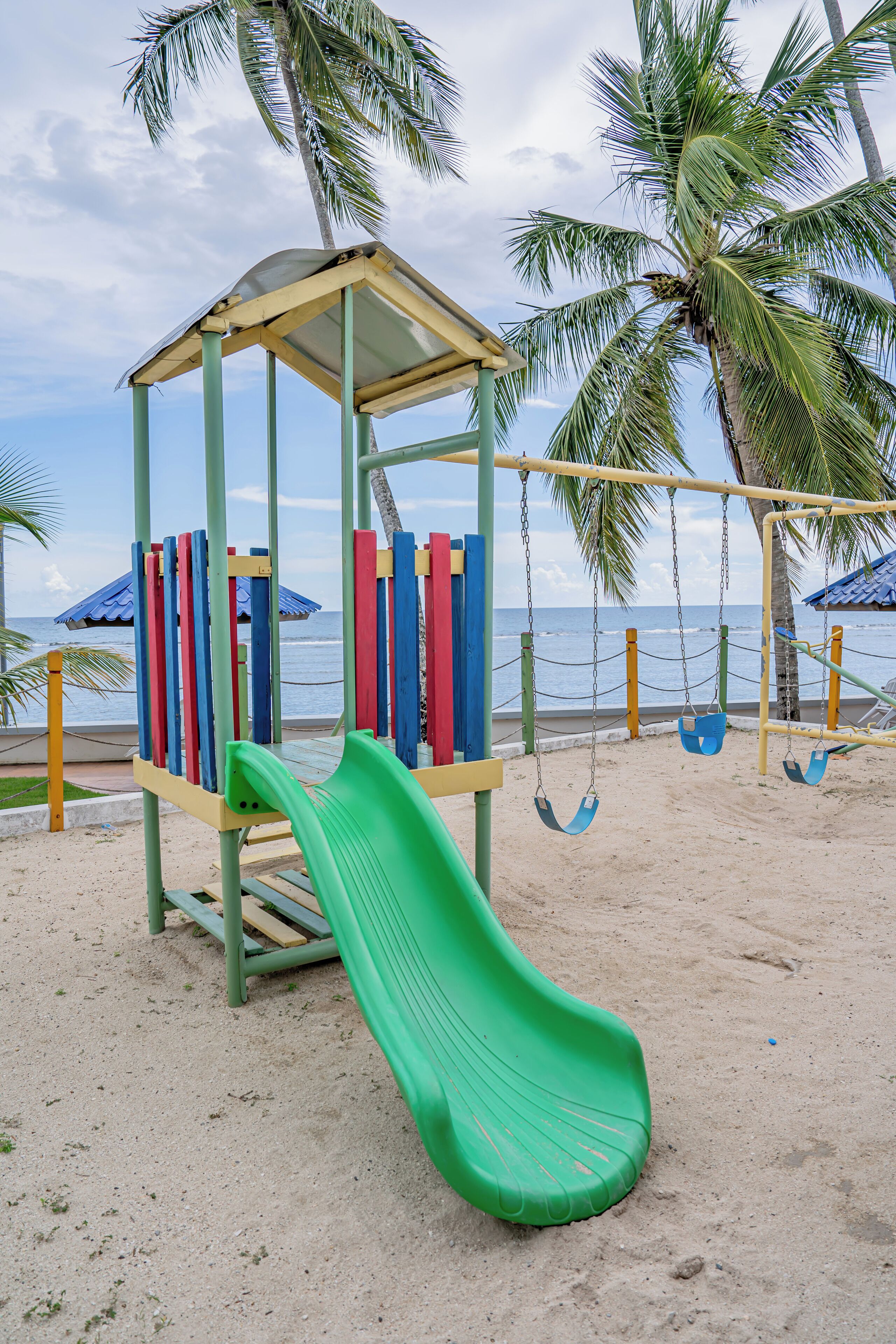 A beach playground with a slide, swings, and a shelter.