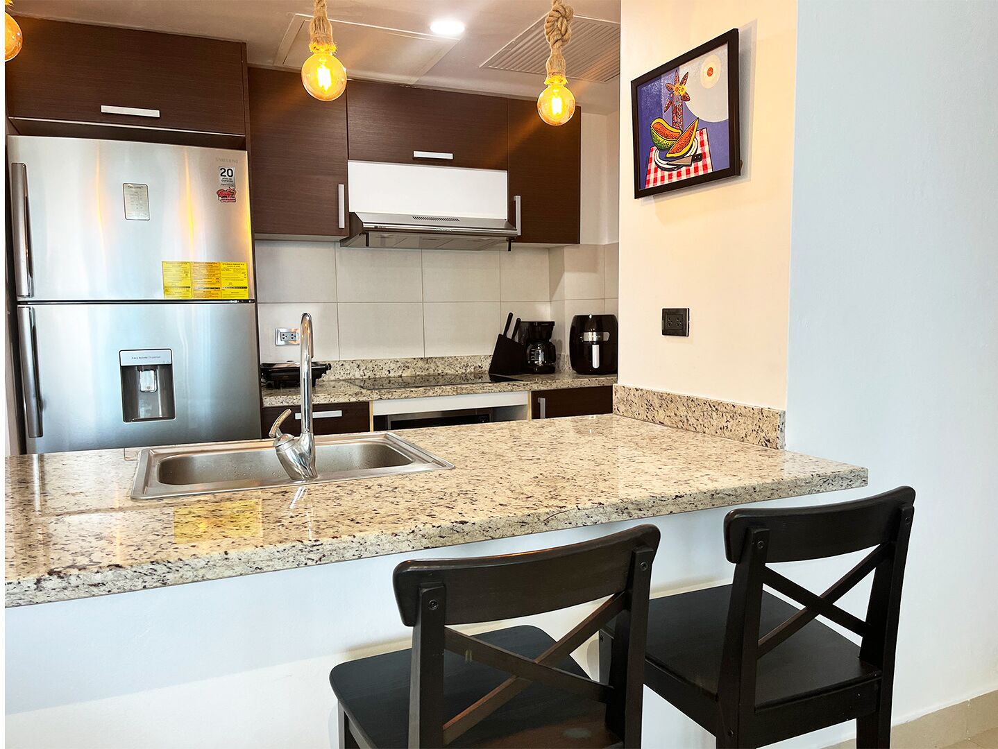 A modern kitchen with stainless steel appliances, granite countertops, and black bar stools.