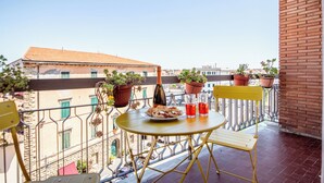 Un balcon avec une table ronde, deux chaises, une bouteille et des plantes en pot.