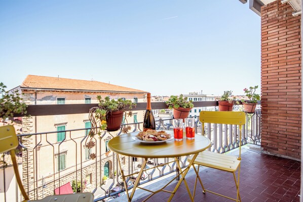 A balcony with a round table, two chairs, a bottle, and potted plants.