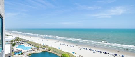 Vista de una playa con piscina, sombrillas y un muelle.