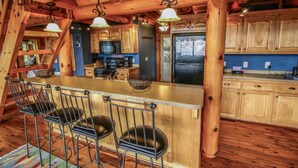 A rustic kitchen with wooden cabinets, a central island with bar stools, and hanging pendant lights. - Cloud 9-Log Cabin, Stunning View, Luxury Hot Tub, Gas Fire Pit, 30 min to Boone (Mountain City)