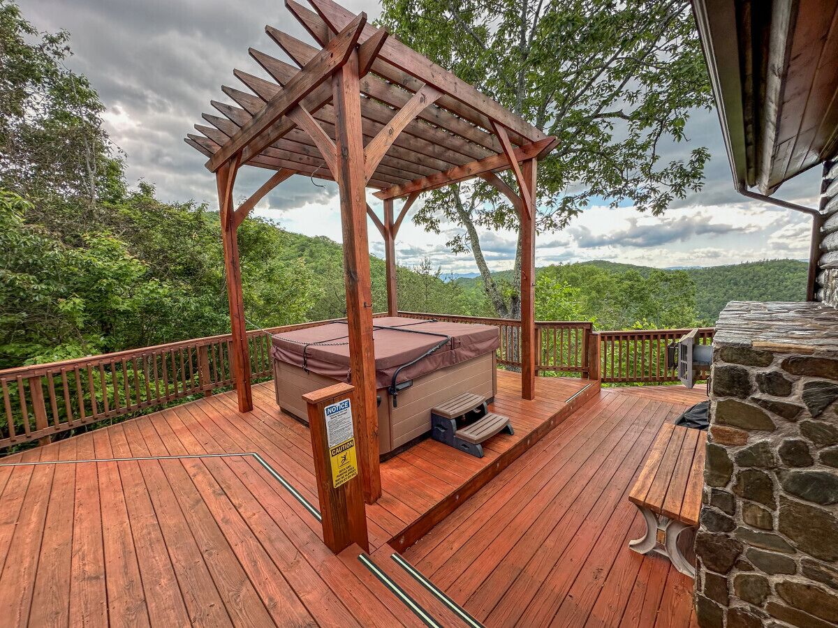 Une terrasse en bois avec un jacuzzi, une cheminée en pierre et une pergola en bois.