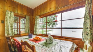 Eine Holzhütte mit Esstisch für zwei Personen, einem Fenster mit Seeblick und einer Orangenschale auf dem Tisch.