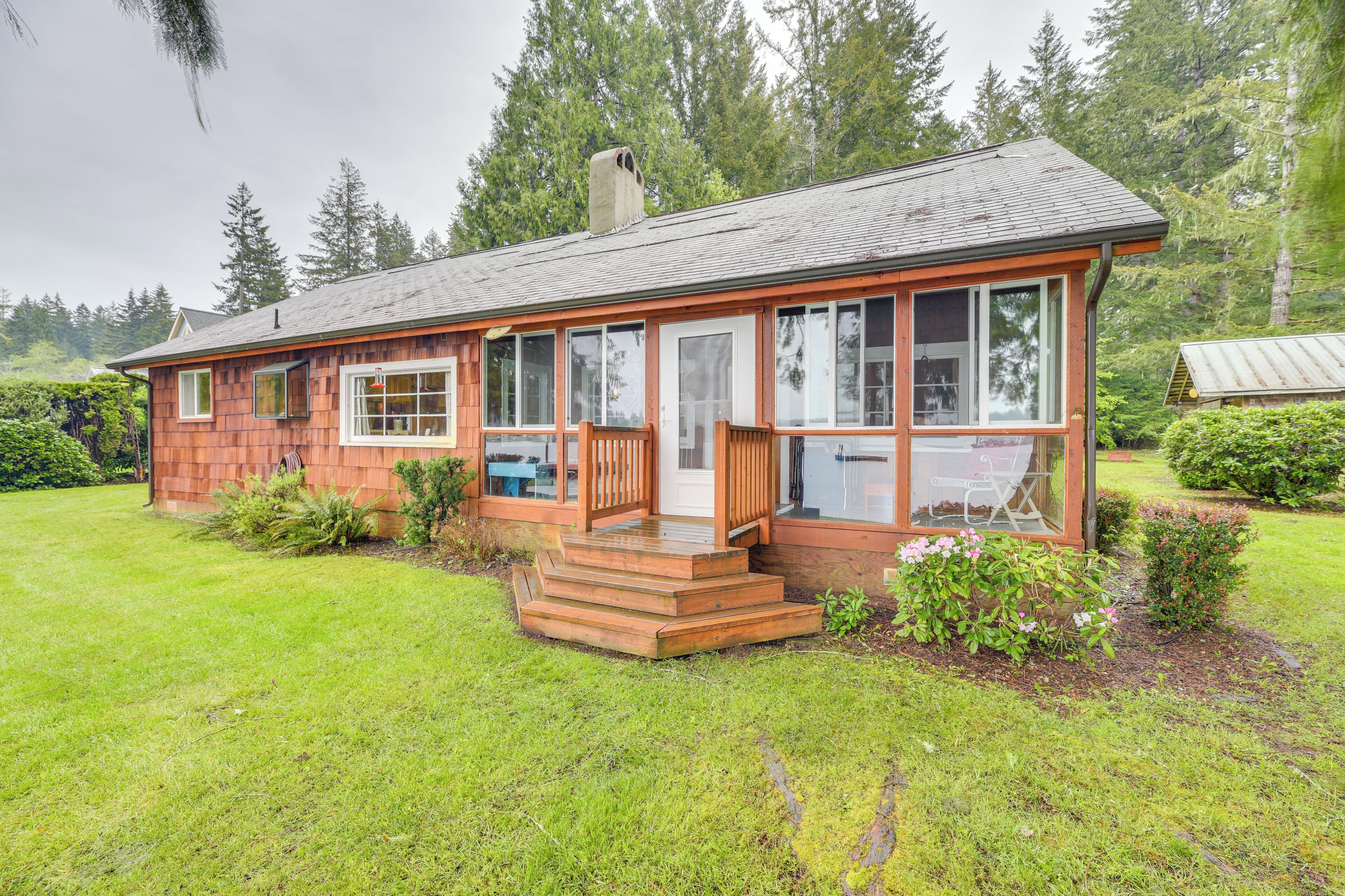 A wooden cabin with a porch, large windows, and a grassy yard.