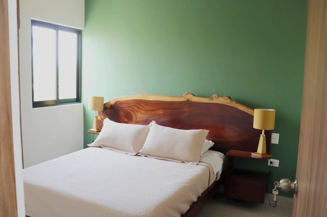 Ein Schlafzimmer mit einem Holzkopfteil, zwei Nachttischlampen, einem Bett mit weißen Leinentüchern und einer grünen Wand.