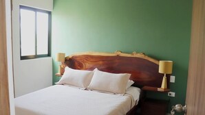Une chambre à coucher avec une tête de lit en bois, deux lampes de chevet, un lit recouvert de draps blancs et un mur vert.