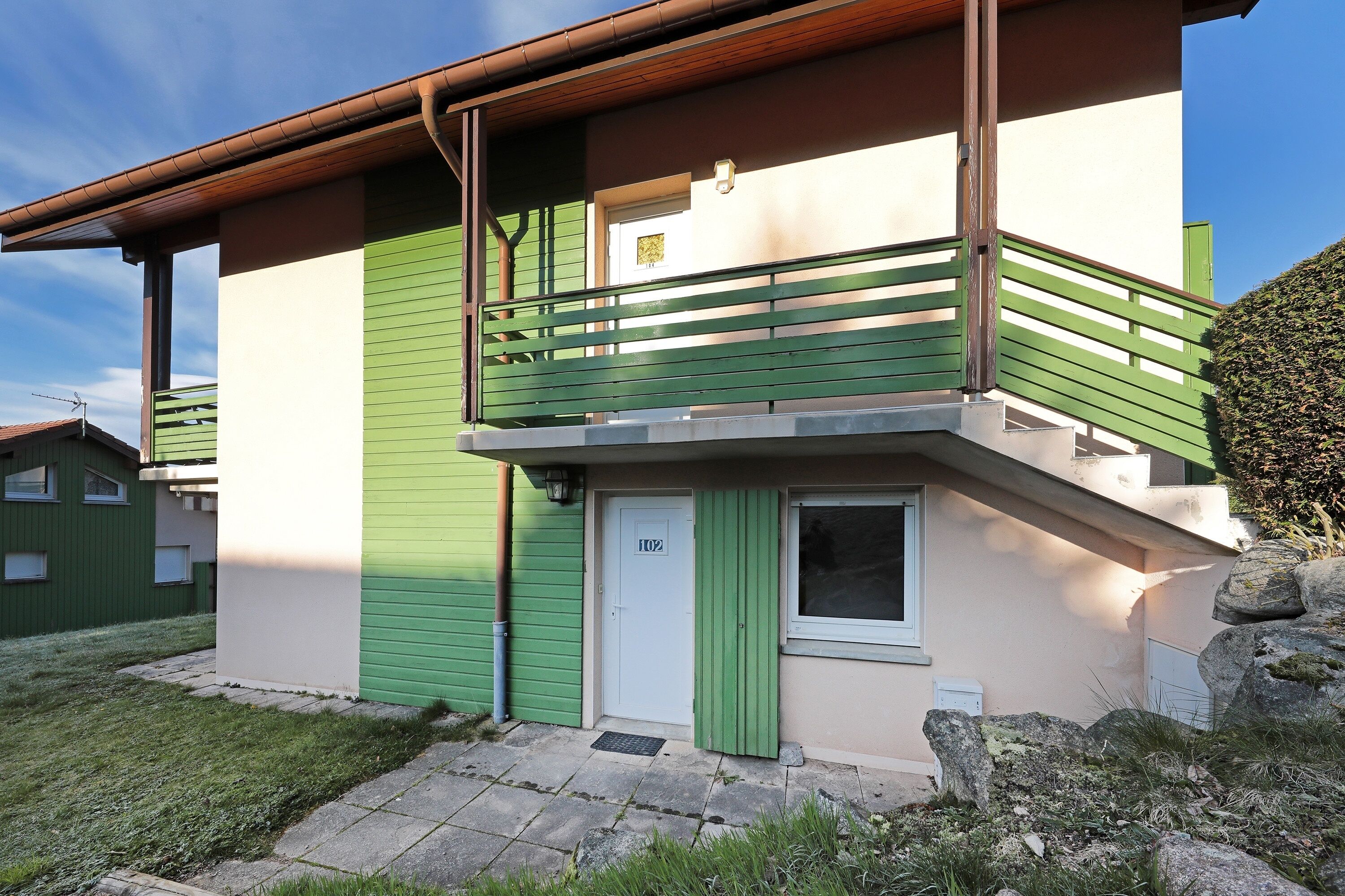 A two-story building with a green exterior and a white door marked "102".