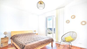 Ein Schlafzimmer mit einem Bett, einem Stuhl, einer Lampe und einem Fenster.