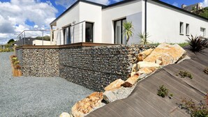 Ein modernes Haus mit Naturstein-Fassade, einer Holzterrasse und blauem Himmel.
