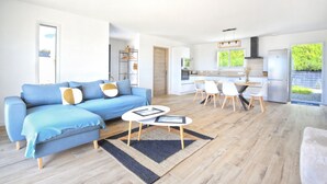 Ein modernes Wohnzimmer mit einem blauen Sofa, einem Couchtisch und einem Essbereich mit weißen Stühlen.