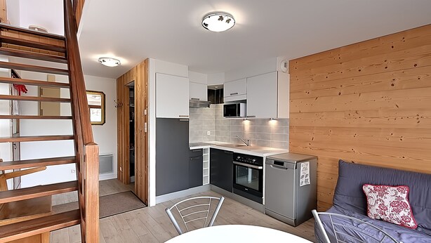 Ett kompakt kök med moderna vitvaror, en matplats med bord och stolar samt en väggpanel i trä.