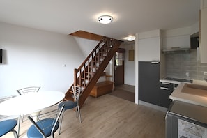 Eine moderne Küche mit Einbauherd, ein Essbereich mit rundem Tisch und Stühlen sowie eine Holztreppe, die in einen anderen Raum führt.