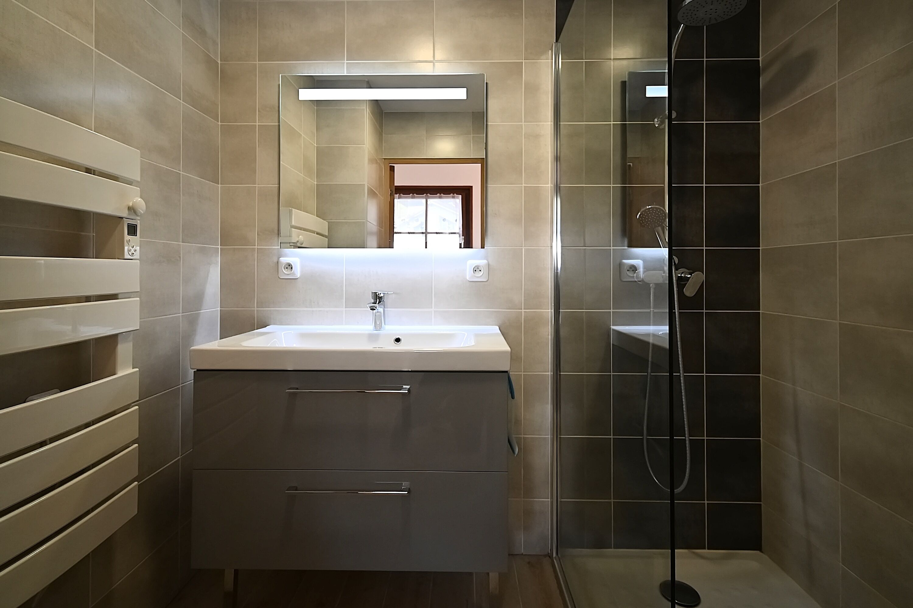 A modern bathroom with a large mirror, a sink, and a shower.
