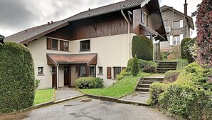 Ett tvåvåningshus med ett sluttande tak, en huvudentré och en liten trädgård framför huset med trappsteg som leder upp till dörren.
