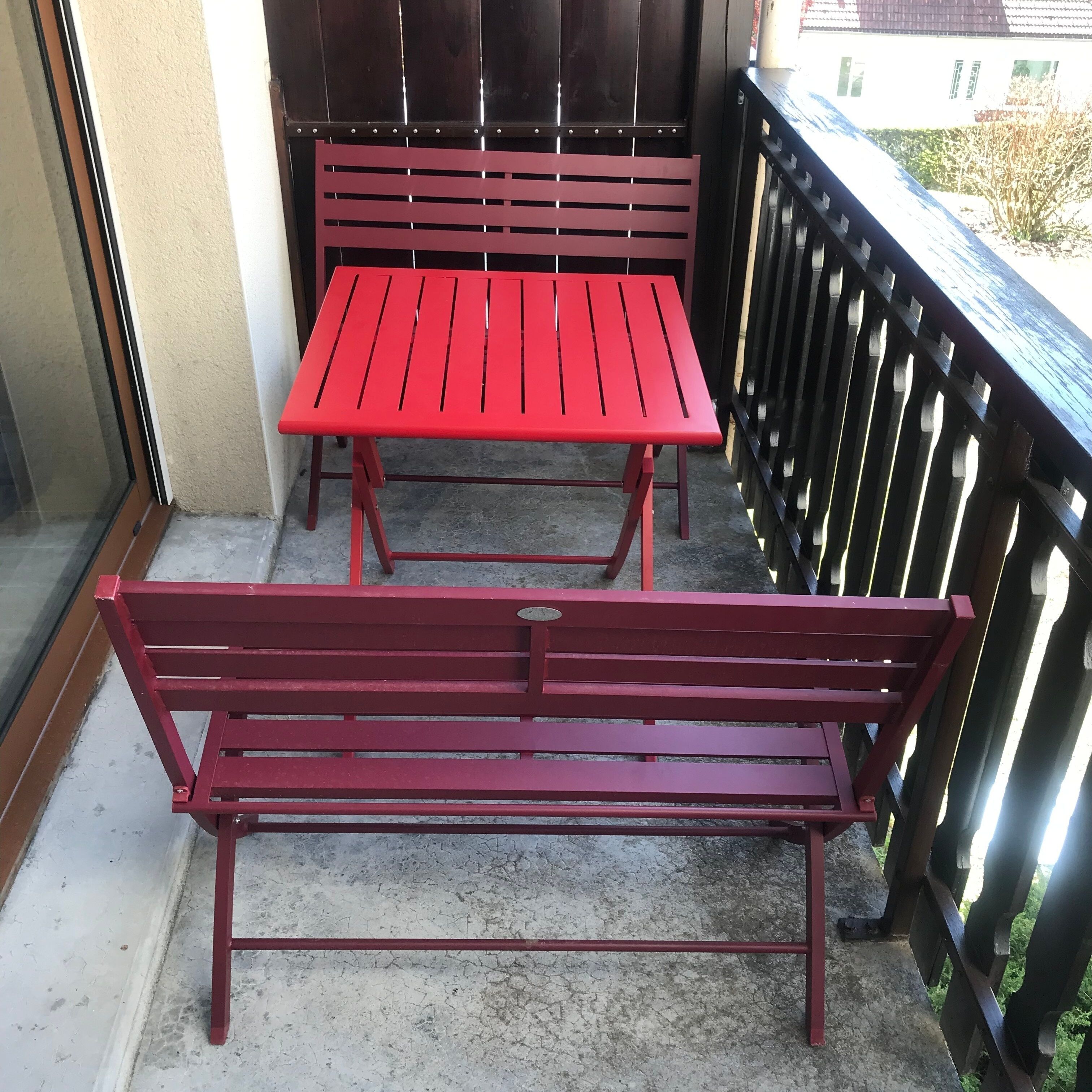 Un balcone con un tavolo e una panca in metallo rosso.