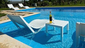 Un área junto a la piscina con sillas de descanso, una mesa y una botella de vino.