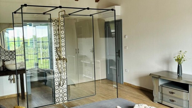 Un dormitorio con separador de vidrio, una cama con almohadas, una mesita de noche y un aparador.