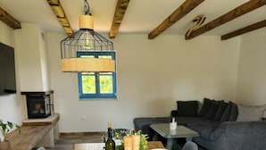 Un comedor con una larga mesa de madera dispuesta para seis comensales, rodeada de sillas tapizadas en gris. Una lámpara colgante con pantalla tejida ilumina la mesa.
