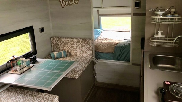 Interni di un camper compatto con angolo cottura, una piccola zona pranzo e una cuccetta.
