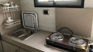 Una cucina compatta con lavello, fornelli e una finestra sopra il lavello.