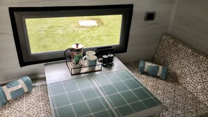 Un’accogliente zona con divano decorato, un tavolino con vassoio contenente un teiera, tazze e un oggetto decorativo. Si intravede una finestra con vista su una zona erbosa.