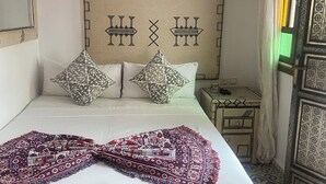 A neatly made bed with patterned pillows and a decorative throw, a bedside table with a lamp, and a wall with geometric patterns. - Zoco Riad (Tangier)