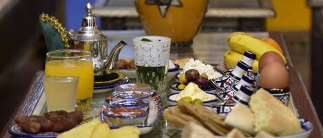 A breakfast tray with various foods and drinks, a vase with flowers, and a decorative wall in the background.