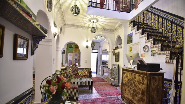 A spacious interior with a high ceiling, ornate arches, a central seating area with a patterned rug, and a staircase with decorative tiles. - Zoco Riad (Tangier)