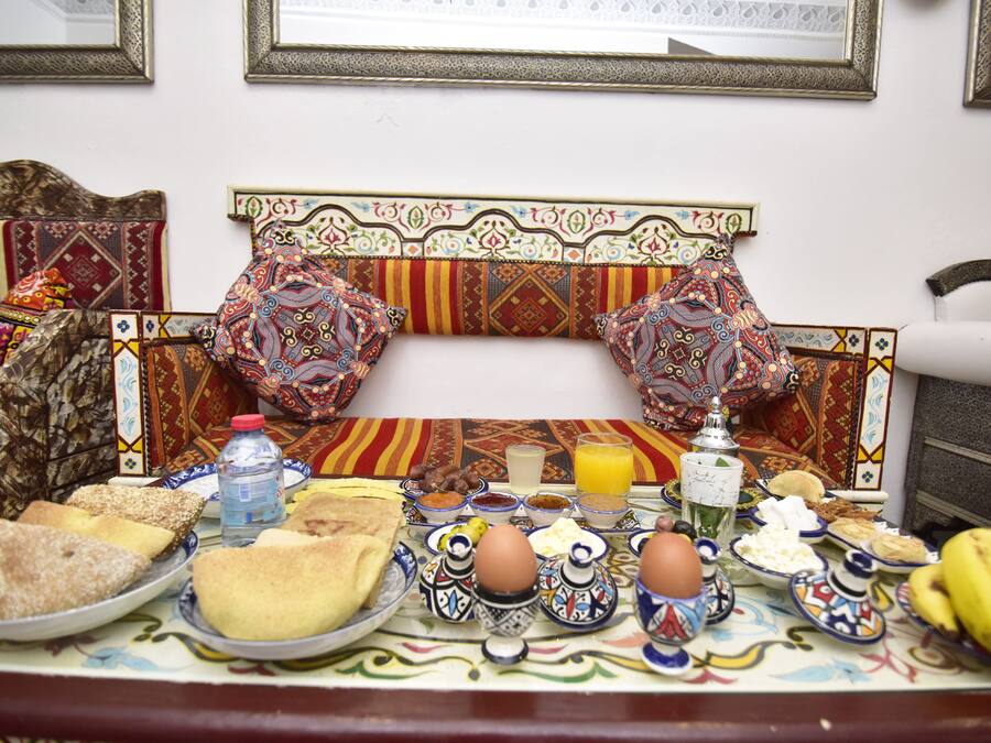Una mesa de desayuno con diversos platos, incluyendo pan, huevos y frutas, sobre un mantel estampado.