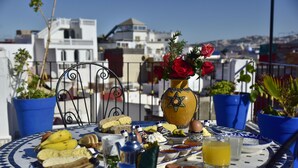 A table with food and drinks, surrounded by potted plants and a decorative vase with roses. - Zoco Riad (Tangier)