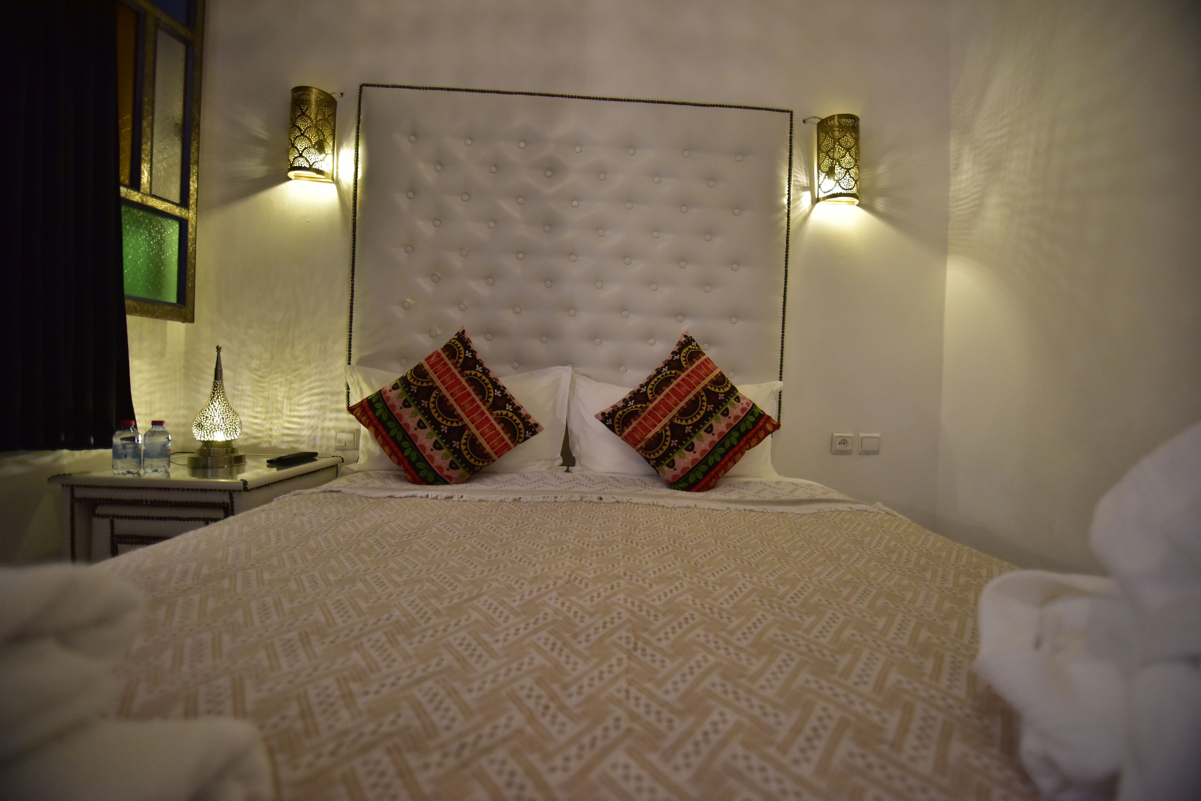 A neatly made bed with patterned bedding, two decorative pillows, and wall-mounted lights on either side.