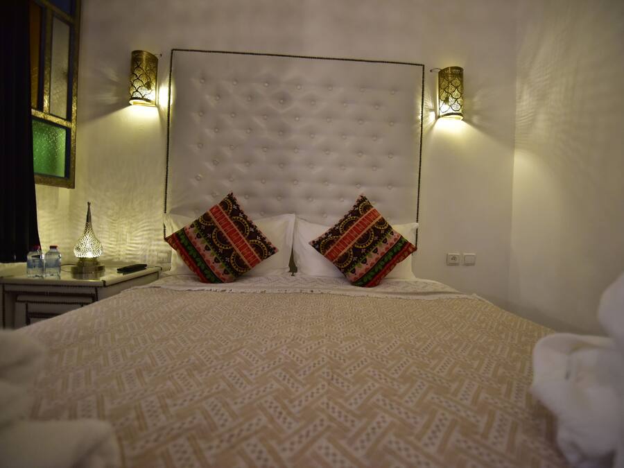 A neatly made bed with patterned bedding, two decorative pillows, and wall-mounted lights on either side.