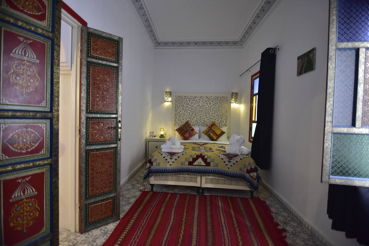 A bedroom with a bed, decorative wall panels, and a red carpet.