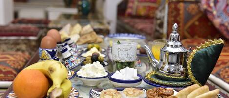 A tray with various food items including fruits, nuts, and pastries, set on a table with a patterned tablecloth.