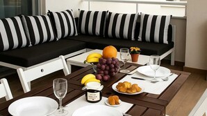 Ein Essbereich mit einem Tisch für zwei Personen, einer Couch mit gestreiften Kissen, einer Obstschale und einer Marmeladenglas.