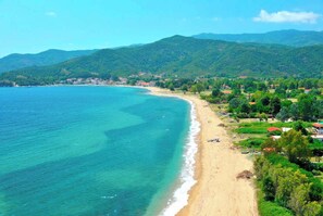 A coastal landscape with a beach, clear blue waters, and green hills in the background. - Aristotelia Gi Ikies - Cozy Pool & Sunny Getaway (Olimpiada)