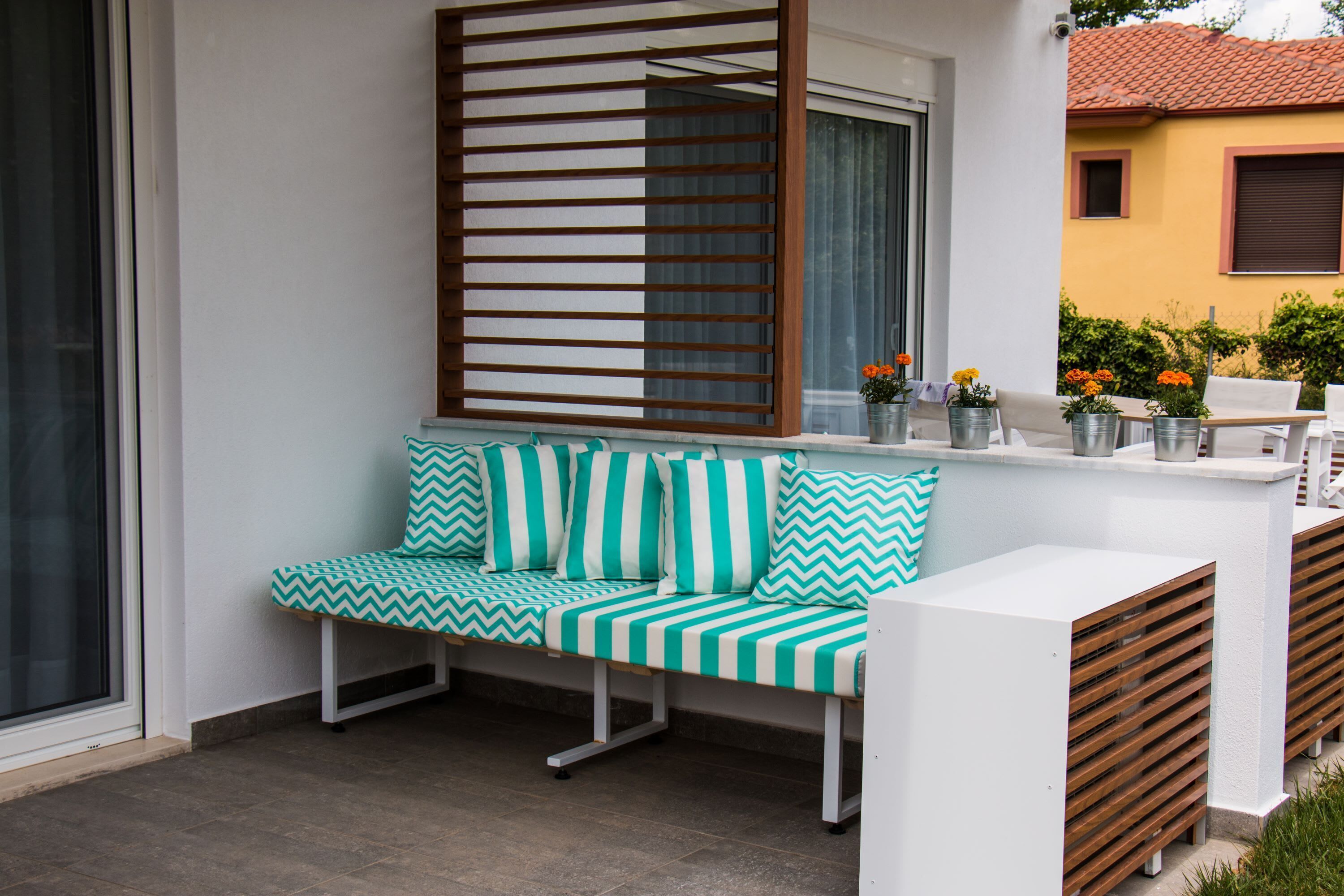 Un espace extérieur moderne, aménagé avec un banc et une table, une cloison en lattes de bois, et offrant une vue sur un bâtiment jaune.