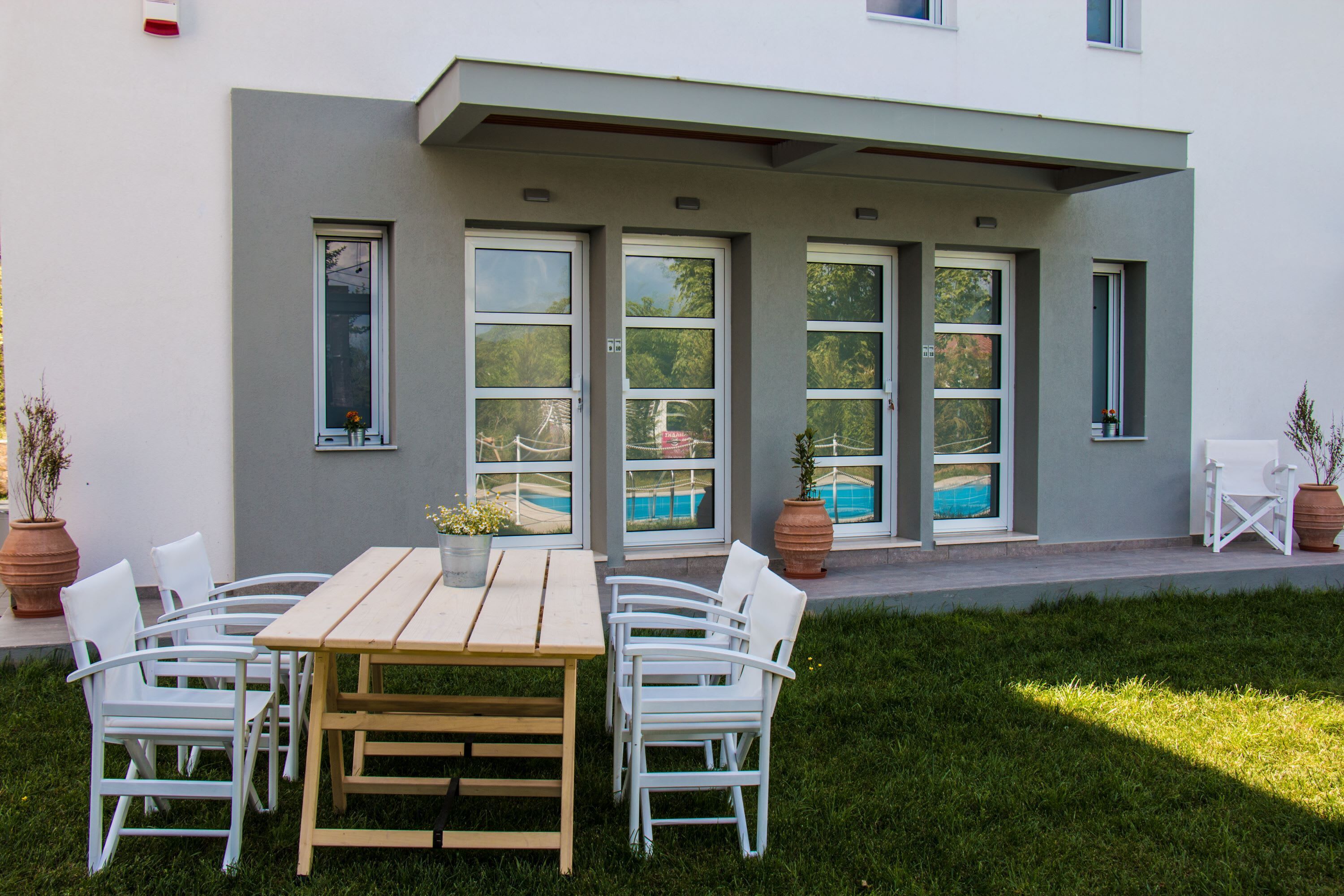 Ein modernes Gebäude mit einer Terrassenfläche, ausgestattet mit einem Holztisch, weißen Stühlen, einem Swimmingpool und Topfpflanzen.