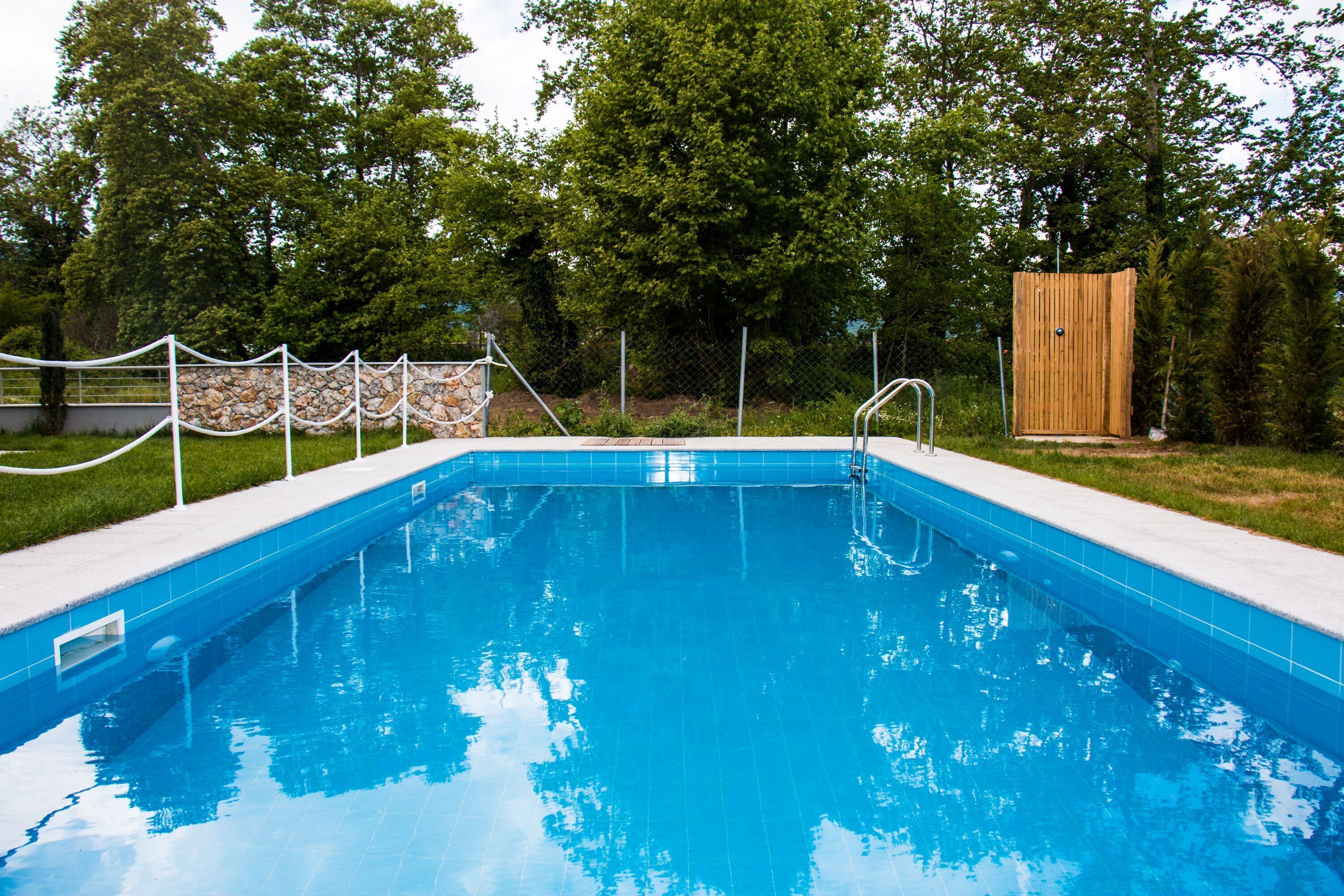 Una piscina rectangular con pared de piedra y cerca metálica.