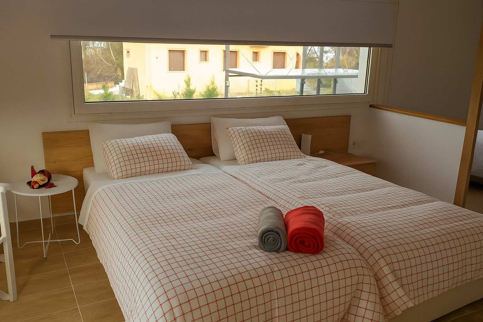 Une chambre à coucher avec un grand lit, deux oreillers, une petite table de chevet et une fenêtre donnant sur des immeubles.