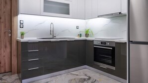 A modern kitchen with dark cabinets, a stainless steel refrigerator, a built-in oven, and a marble backsplash.