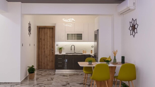 A modern kitchen with a central island, a dining area with green chairs, and a marble floor.