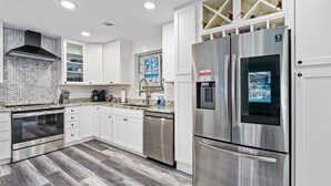 A modern kitchen with white cabinets, stainless steel appliances, and a wooden floor. - Pool Oasis 2 Blocks from Beach (Port Orange)