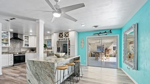 A modern kitchen with a marble island, bar stools, and a ceiling fan. - Pool Oasis 2 Blocks from Beach (Port Orange)